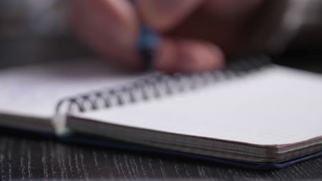 close up of man's hands writing in spiral notepad placed on wooden black desktop