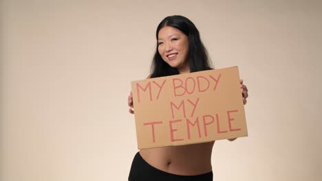 검은 속옷을 입은 미소 짓는 플러스 사이즈 여성이 스튜디오에서 춤을 추고 배너를 들고 있습니다.
