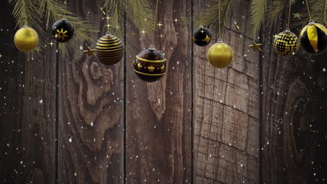 swinging black and gold christmas baubles over falling snow on dark wood background