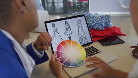 Diverse-female-and-male-designers-discussing-fashion-designs-on-laptop-and-colour-wheel-in-studio