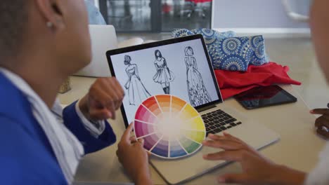 diverse female and male designers discussing fashion designs on laptop and colour wheel in studio