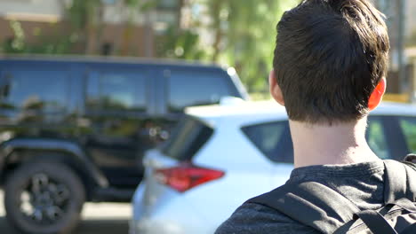 a young caucasian male student with a backpack for school walks through a parking lot