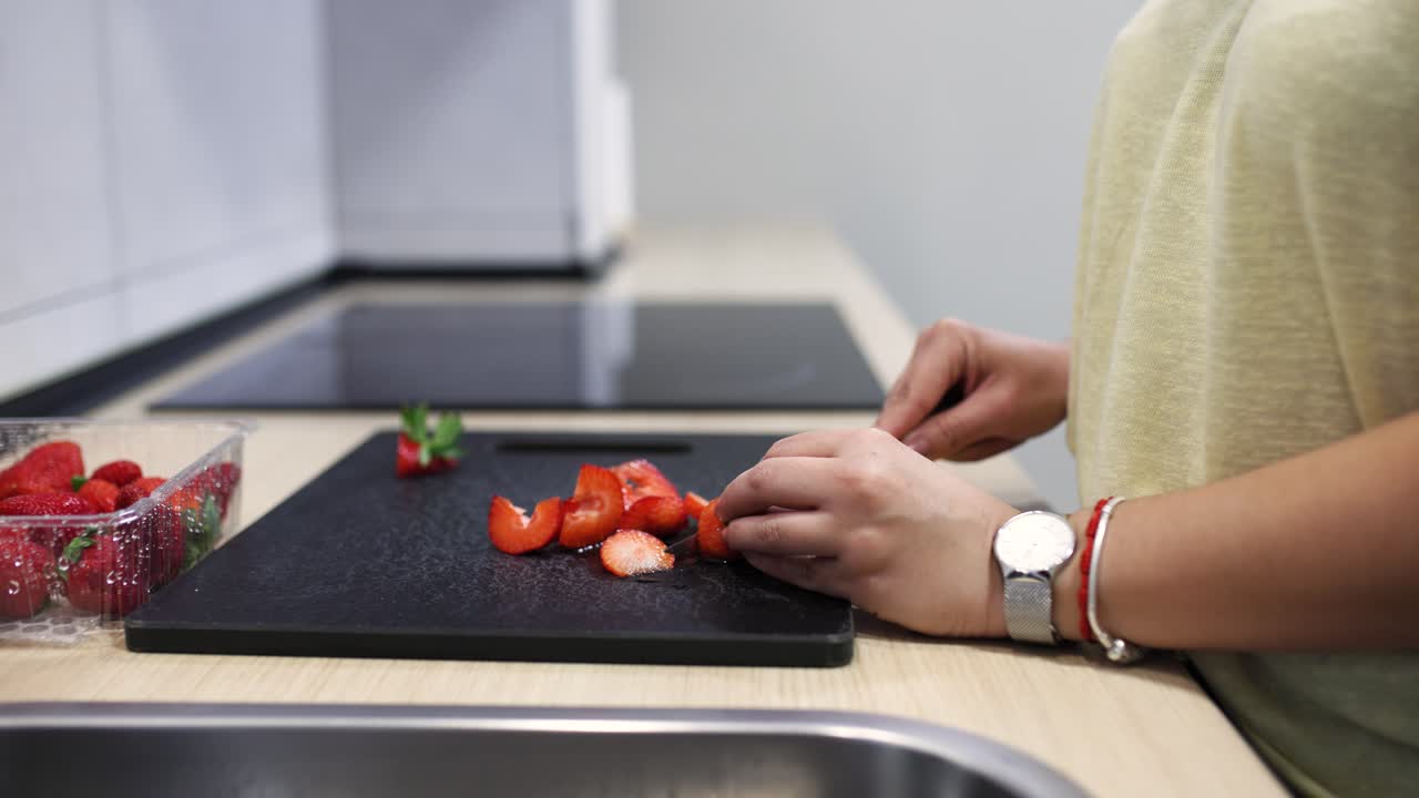 Woman slicing strawberries on cutting board in modern kitchen