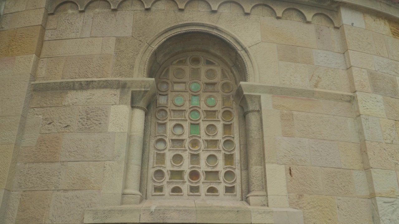 Primo piano statico di una finestra ad arco in pietra ornata con grata circolare decorativa sulla facciata di una chiesa storica