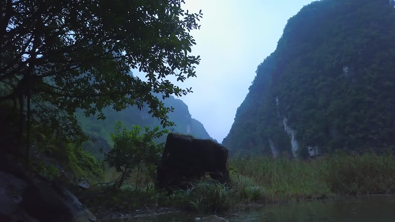 Cinematic drone footage of majestic limestone peaks in misty and foggy weather. Ricefields in wild jungle in the spring with boat tour canal in Tam Coc, Ninh Binh, Vietnam