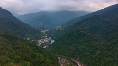 fotografía de avión no tripulado de un río y un pueblo en el valle entre las verdes montañas de wulai 烏來區, taiwán - fotografía amplia