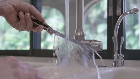 a caucasian male is rinsing a knife in a home kitchen