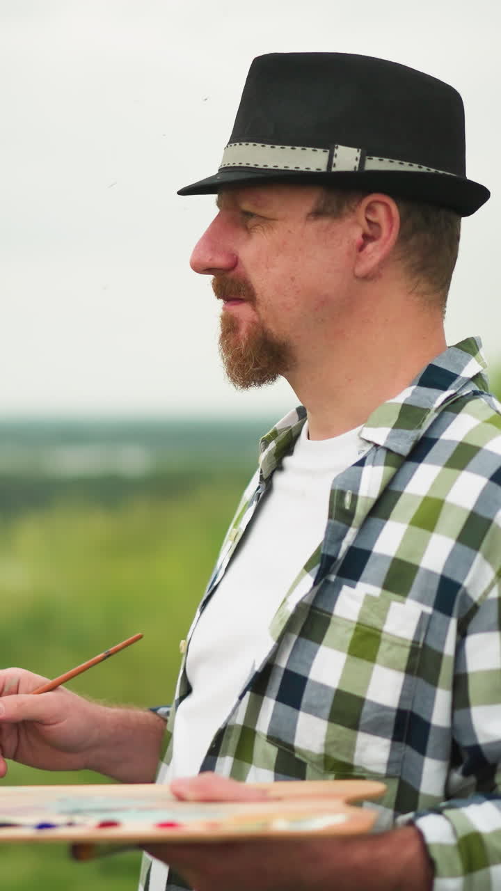 모자와 체커드 셔츠를 입은 화가 한 명이 호수 근처의 조용한 풀에 초점을 맞추고 있으며, 팔레트와 페인트 브러쉬를 들고 있습니다.