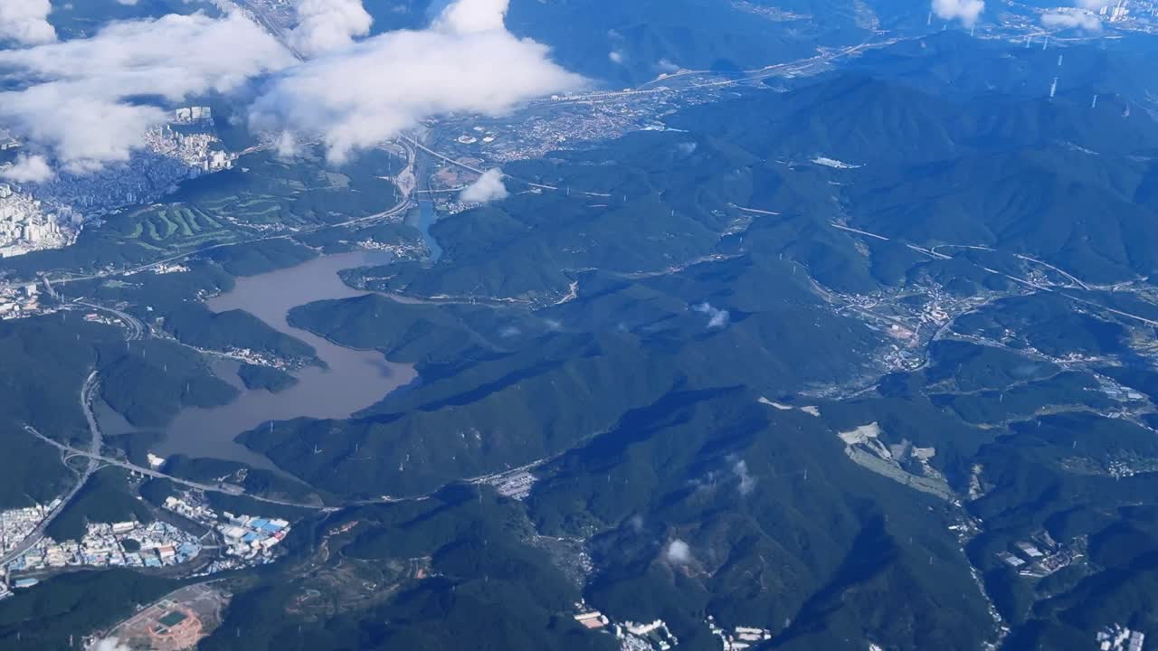 A city with nearby mountains and a lake under a partly cloudy sky , aerial view