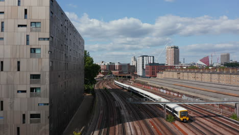 Forward-tracking-of-passenger-train-driving-on-multi-track-railway-line-leading-around-modern-designed-apartment-house.-London,-UK