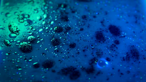 liquid with oil and black spots on surface swirling, lit by neon colors, close up