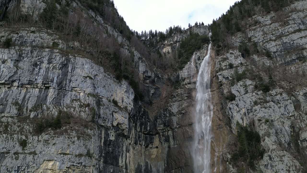 Vannkaskade som faller bratt fra fjellene og grå himmel