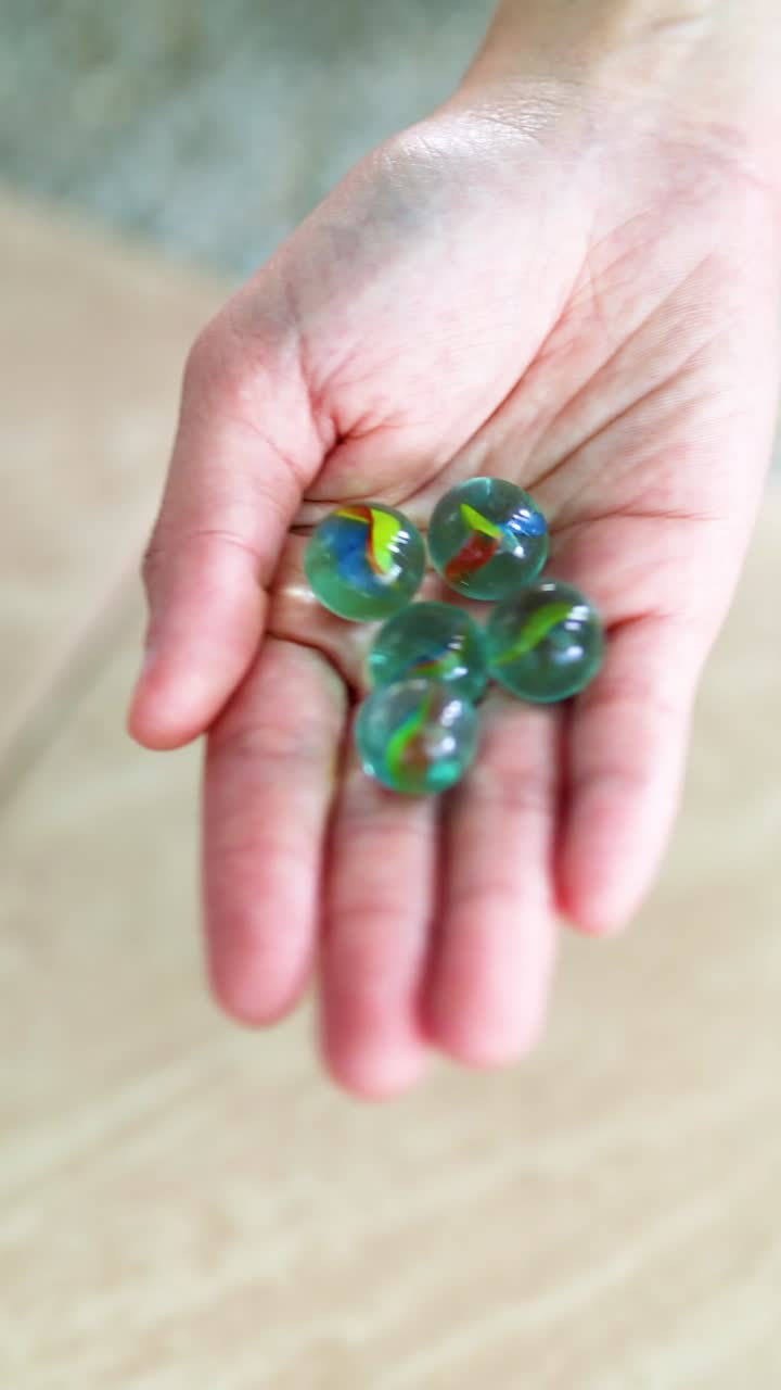 una mano sostiene suavemente los mármoles verdes sobre un piso de azulejos con luz natural, creando una atmósfera serena y enfocada