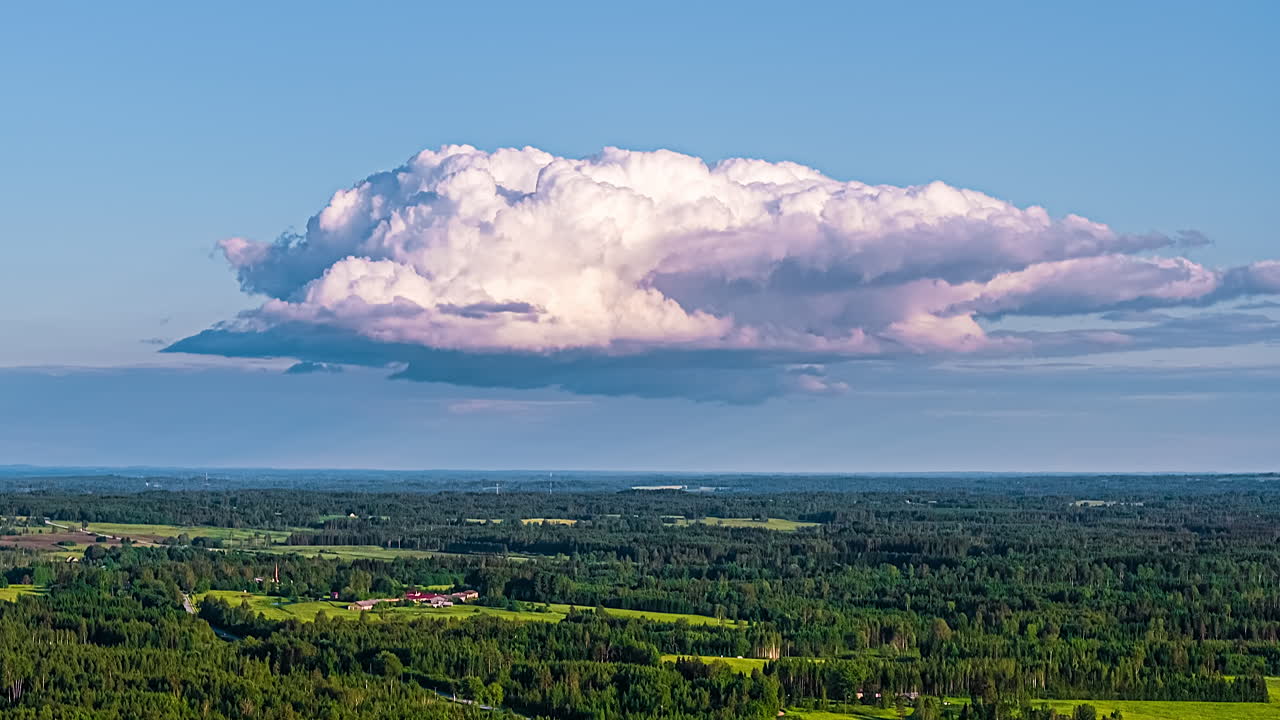 Timelapse of a large cloud drifting over a green forest landscape
