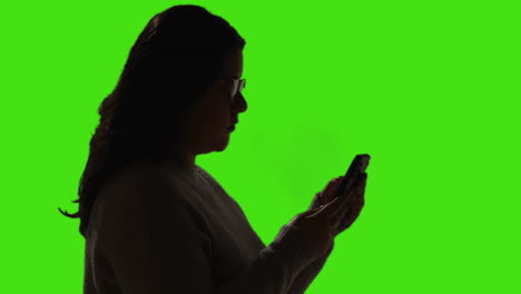 woman looking at text message or browsing online on mobile phone against green screen background with low key lighting