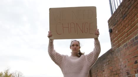 Strong-woman-walking-in-protest-holding-a-sign-for-change-on-a-street-low-angle