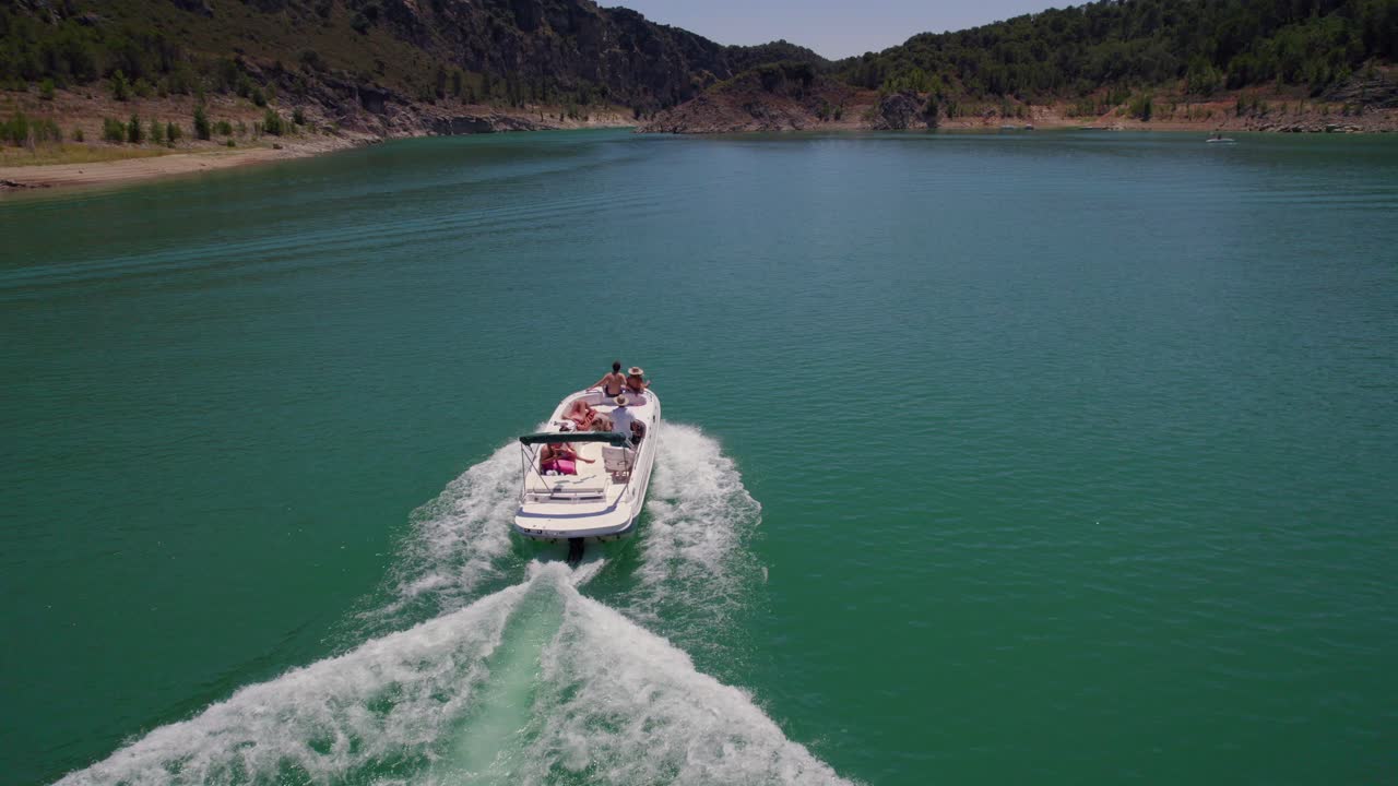 Drone following a boat with a group of friends sailing in a turquoise water reservoir in summertime