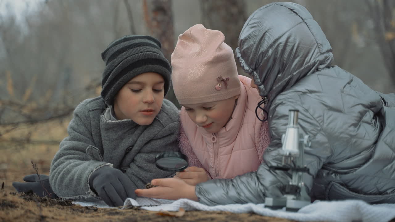 Kids interested in nature and science. Little girls and boy looking through a magnifying glasss and microscope in the forest. Close-up.