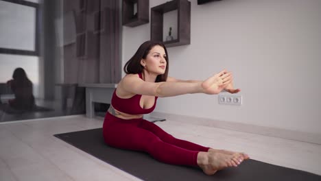 Woman-is-training-at-home-at-morning,-sitting-on-floor-and-stretching-hands-forward
