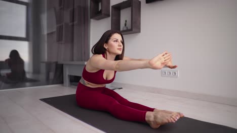 woman is training at home at morning, sitting on floor and stretching hands forward