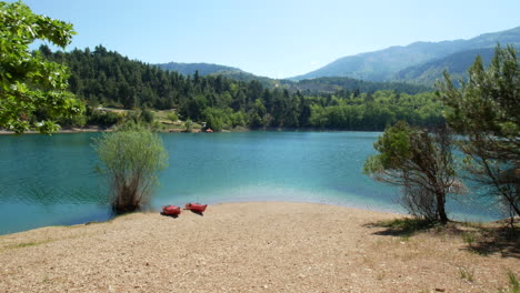 Zooming-into-the-scene-on-the-shore-of-Lake-Tsivlou-where-two-kayaks-can-be-seen-with-the-beautiful-clear-blue-waters-and-open-sky-with-green-covered-mountains