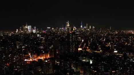 drone night shot of the new york city manhattan skyline, empire state building and housing projects at night