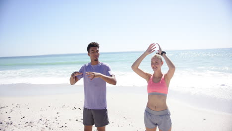 young biracial man and caucasian woman stretch their arms up on a sunny beach