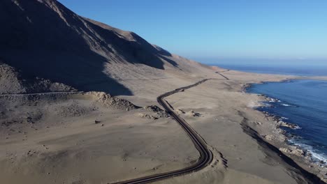 Black-tarmac-highway-through-coastal-desert-sand,-ocean-coast-in-Chile