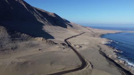 black tarmac highway through coastal desert sand, ocean coast in chile