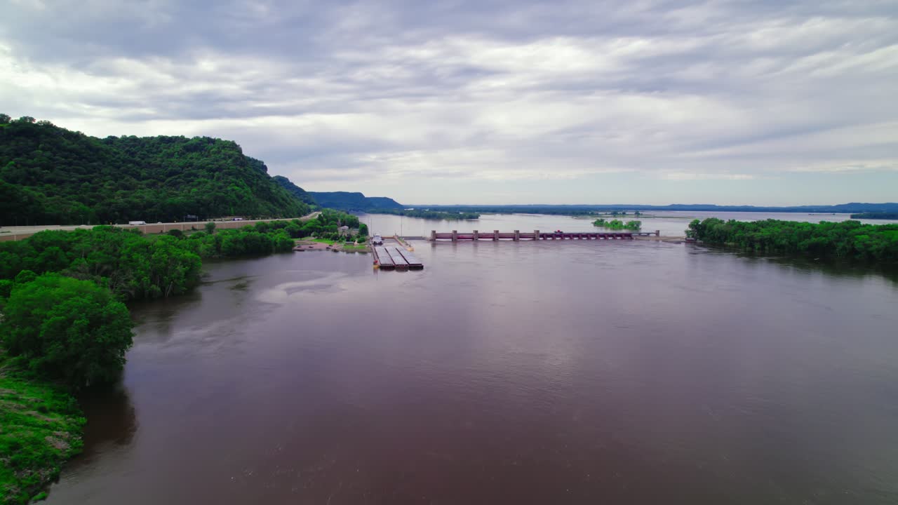 Barge navigating through lock and dam system on the Mississippi River near La Crescent, Minnesota, aerial perspective.
