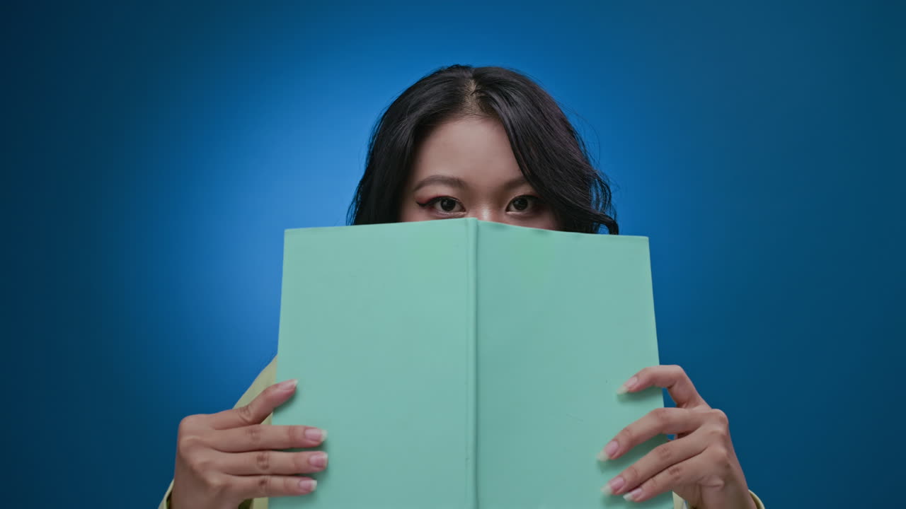 Brunette Holding Book near Face and Smiling at Neon Background