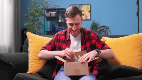 a teenage college boy unpacks a package. the happy young man opens the cardboard box and takes out a new console pad. the teenage male student is happy to receive the package