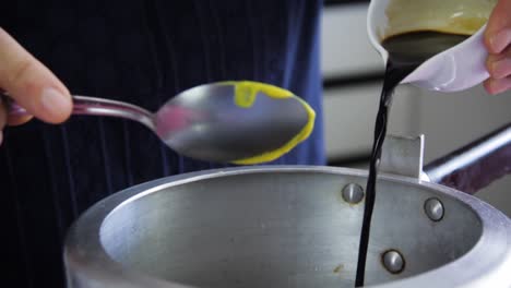 Female-hands-pouring-soy-sauce-inside-a-pressure-pan-with-a-spoon-in-hands