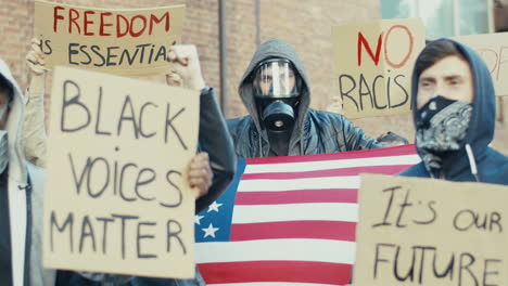 caucasian man in gas mask holding united states flag in a protest against racism with multiethnic group of people in the street