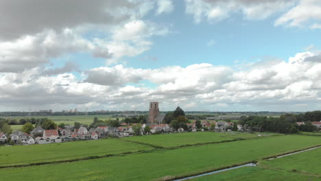 Aerial-approach-of-the-village-of-Ransdorp-with-its-agrarian-surroundings-just-outside-of-Amsterdam-in-The-Netherlands-against-a-blue-sky-with-clouds