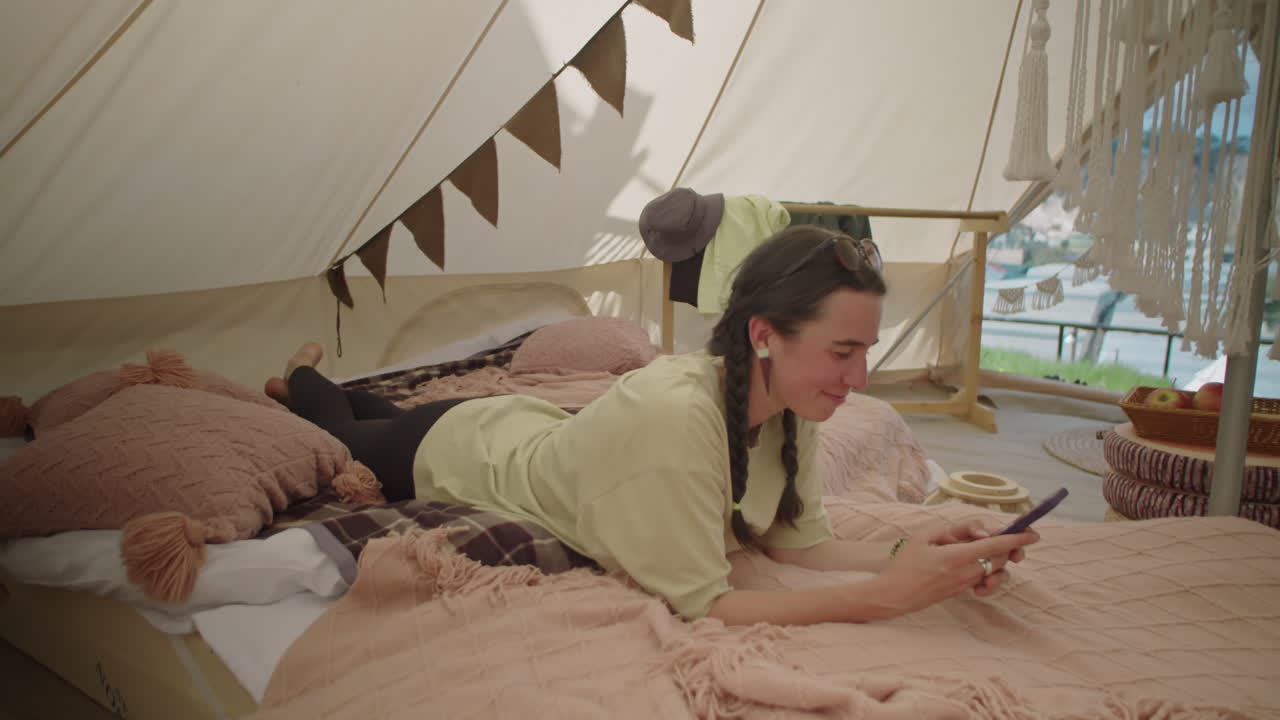 Female Tourist Lying in Glamping Tent and Texting on Phone
