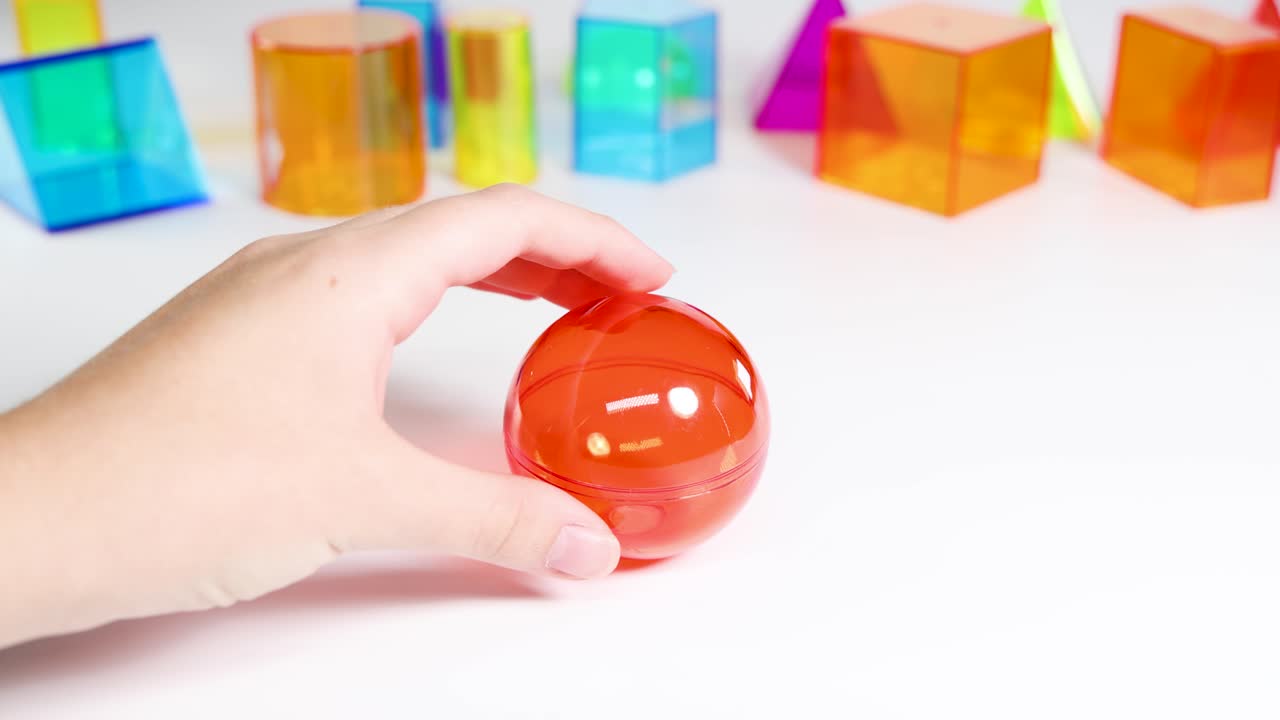 Hands interact with vibrant geometric shapes on a white table, highlighting educational play with colorful prisms and spheres