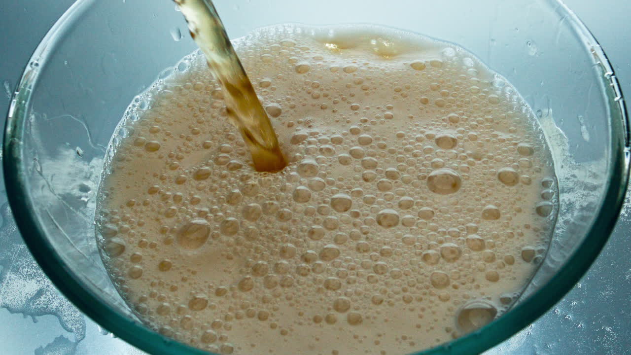 Primo piano di un getto di birra artigianale che si versa in un bicchiere. Liquido alcolico fresco che forma schiuma nel recipiente.