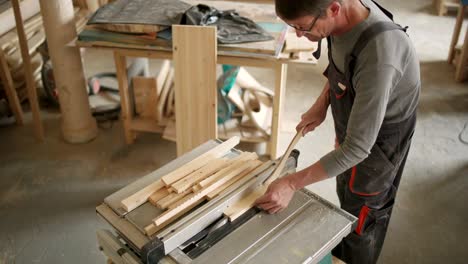 high angle view of experienced mature furniture maker cutting wooden planks with circular saw in workshop