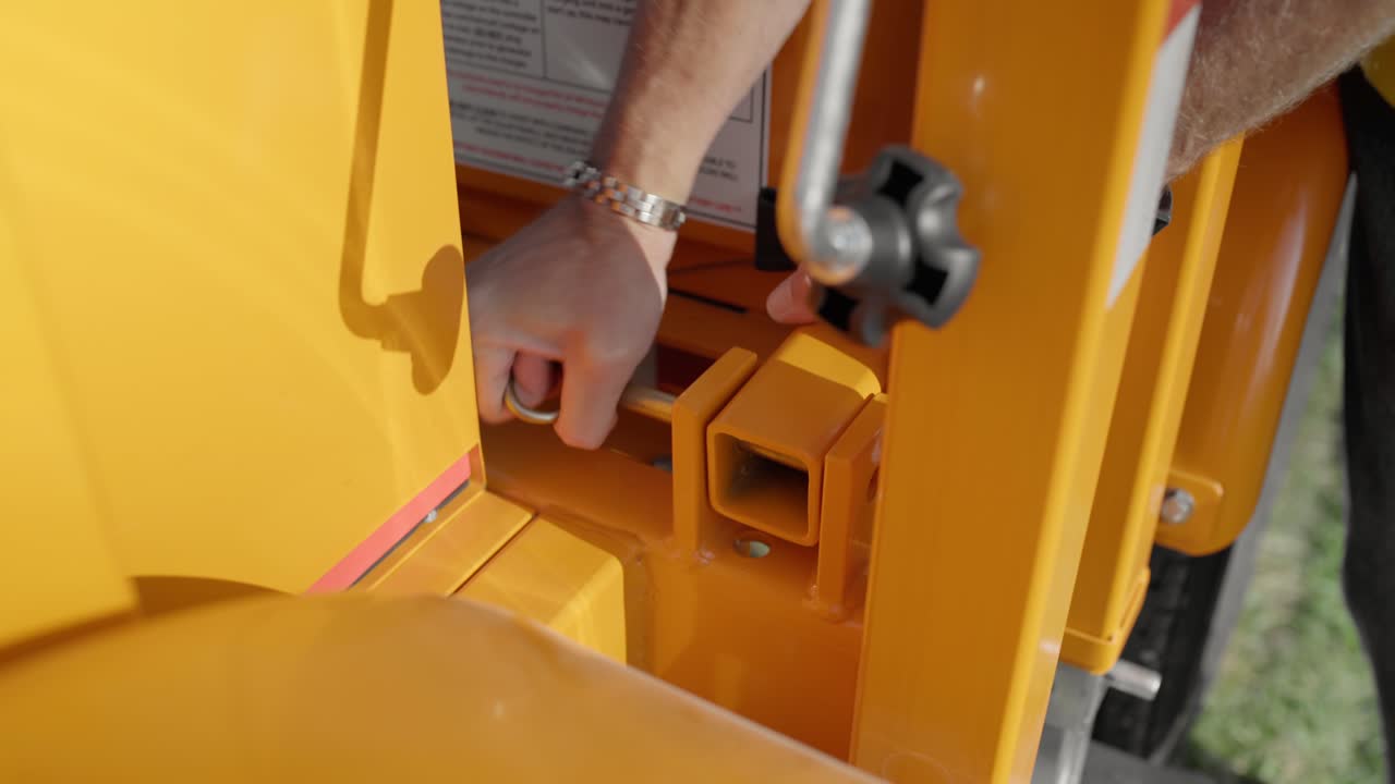 Le mani di un operaio edile rimuovono un perno dal braccio di un segnale di stop mobile da cantiere.