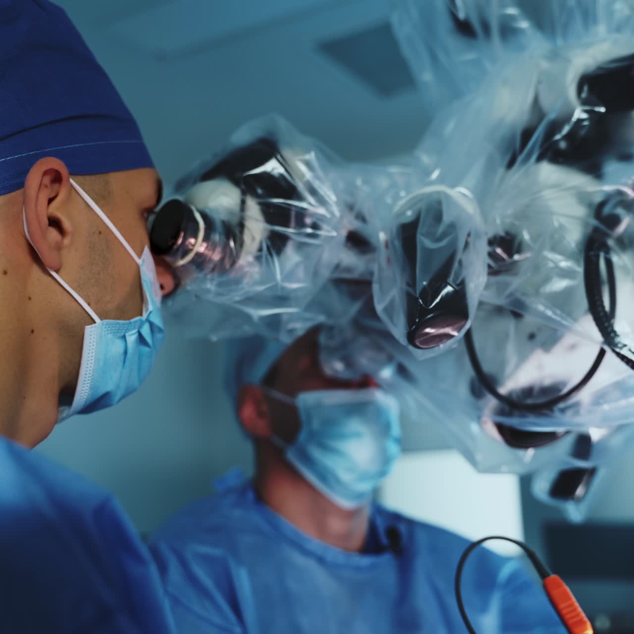 Advanced powerful microscope is used at surgery. Neurosurgeons look at binoculars of equipment covered in plastic. Modern surgery room backdrop