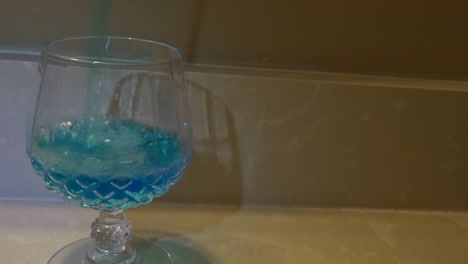 frontal shot of blue liquid being poured into a wine glass