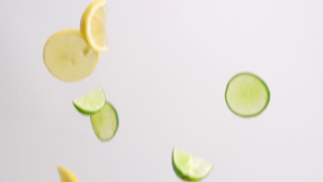 Lemon-and-lime-citrus-fruit-wedges-and-slices-falling-through-the-air-on-white-backdrop-in-slow-motion