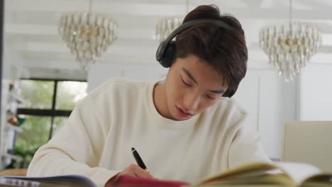 asian male teenager with headphones learning and sitting in living room