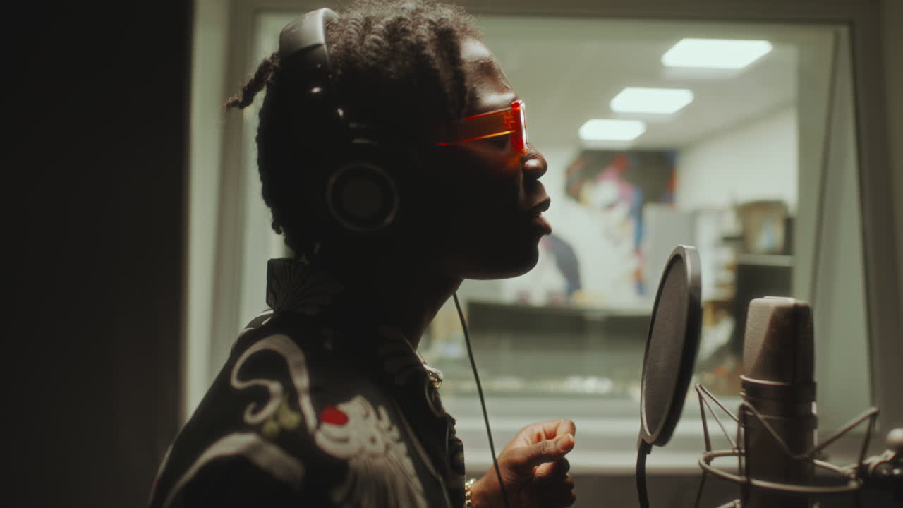 Black Singer in Headphones Recording Vocals in Soundproof Studio Booth