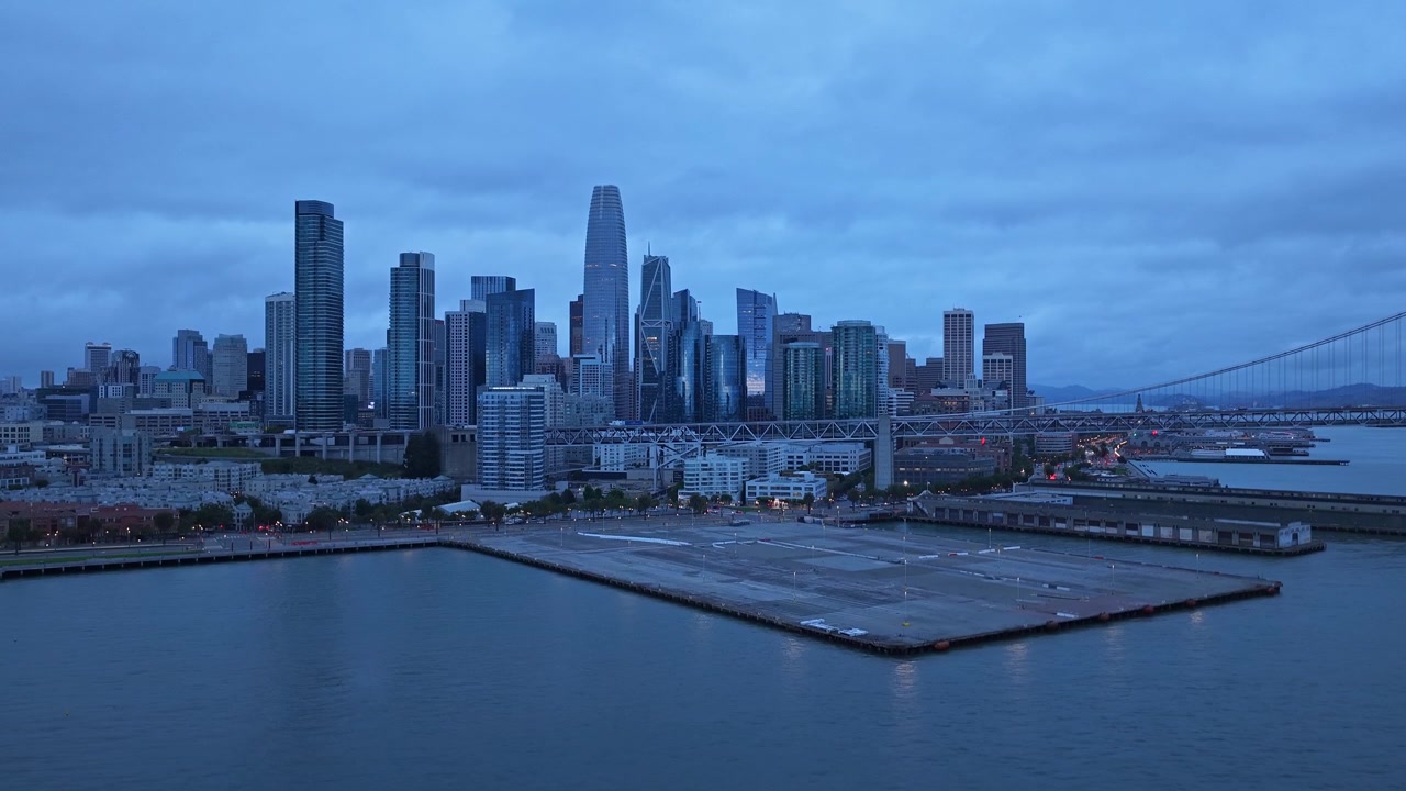 Vista drone del moderno skyline di San Francisco e del Bay Bridge al tramonto, con grattacieli iconici, acque calme e un'illuminazione suggestiva dell'ora blu per immagini urbane cinematografiche