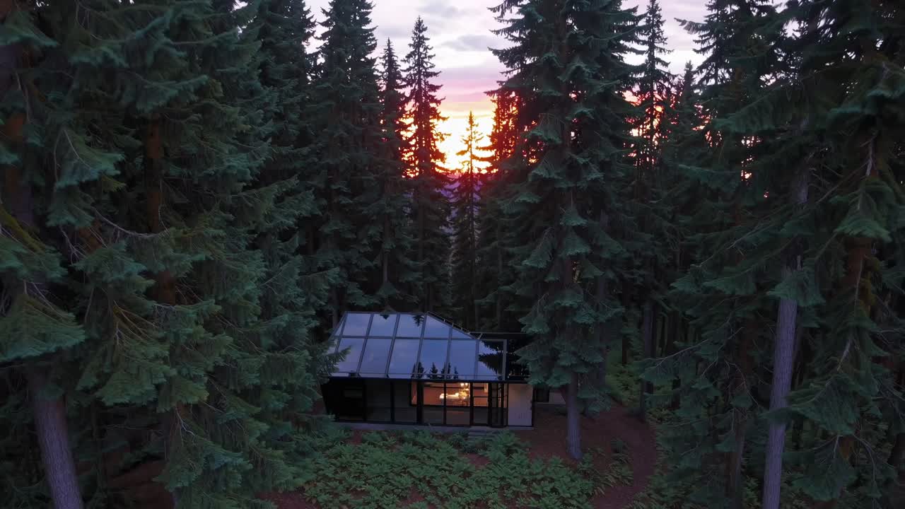 Modern glass cabin nestled among tall trees, capturing the vibrant sunset glow, showcasing the serene beauty of nature and architectural harmony