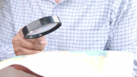 person examining world map with magnifying glass