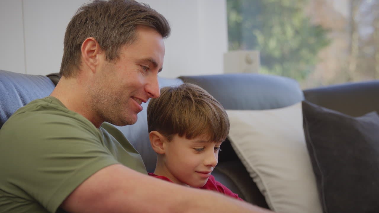 padre e hijo sentados en el sofá en casa en pijama juntos mirando la computadora portátil - filmado en cámara lenta