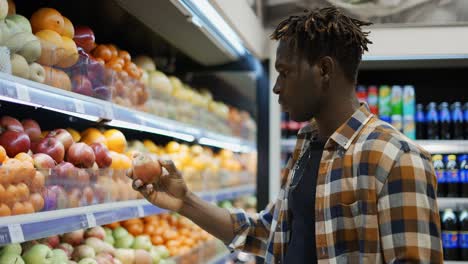 hombre guapo parado en el supermercado y eligiendo manzanas